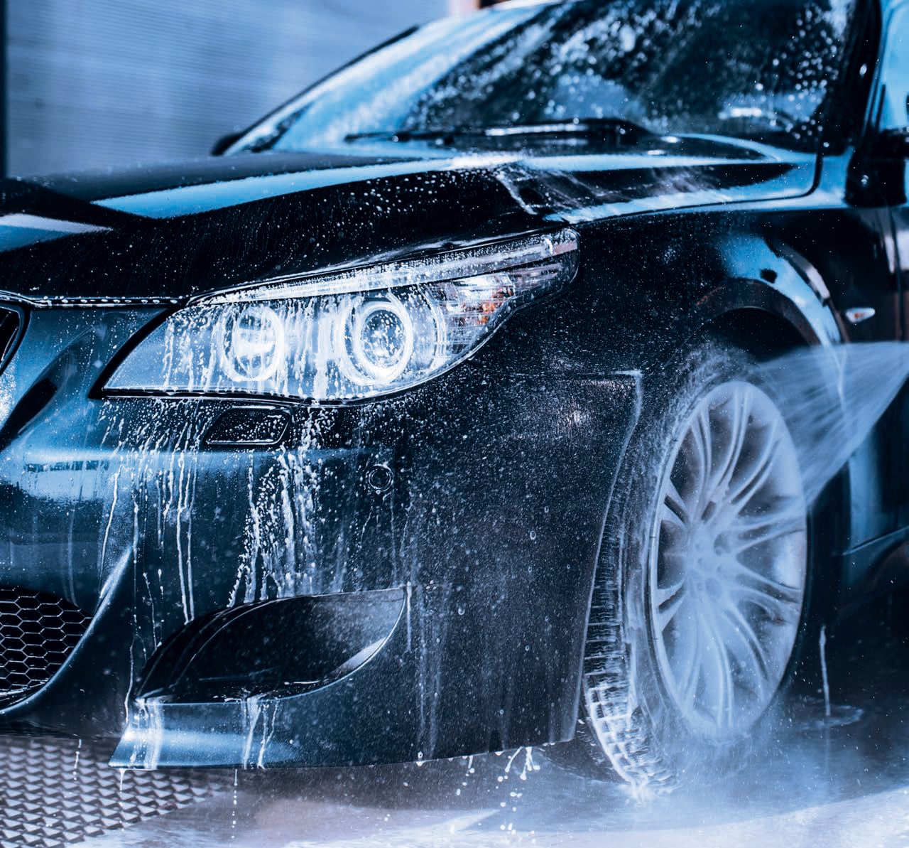 Coche negro siendo lavado a presión con agua y espuma